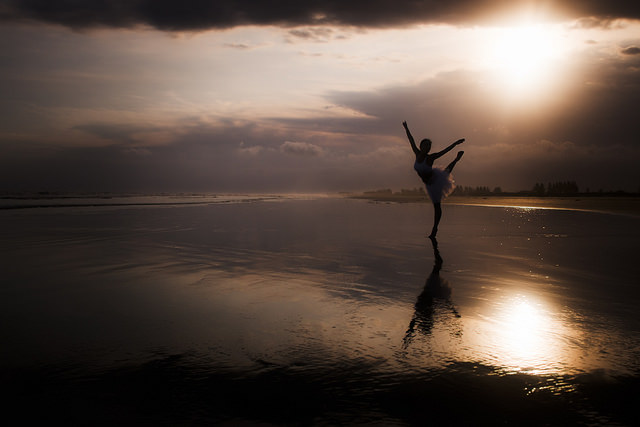 Une danseuse en pleine nature, sur du sable mouillé et lors d'un coucher de soleil.