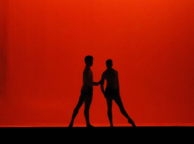 Photographie d'un ballet ou l'on distingue deux ombres sur fond rouge.