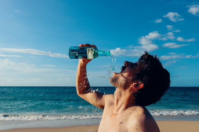 Un homme boit de l'eau devant la mer.